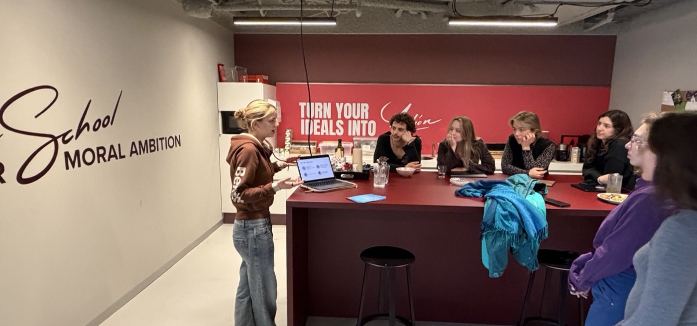 Someone presenting from a laptop to colleagues seated along the red kitchen bar.
